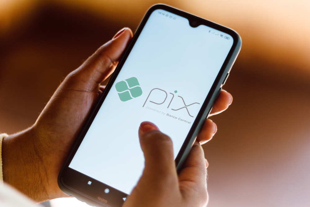 Uma pessoa segura um celular e mostra na tela a logo do Pix, pagamento instantâneo.