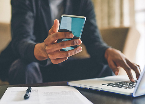 Hotline - Pessoa mexendo no computador e verificando informações no celular