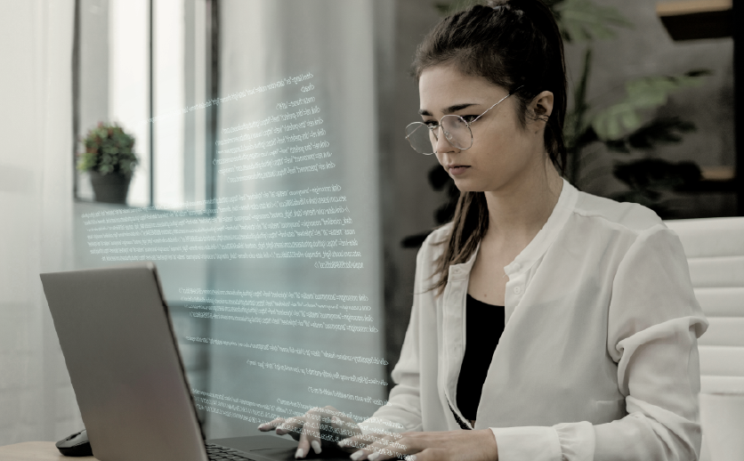 Mulher executiva branca digita em um notebook em um ambiente corporativo.