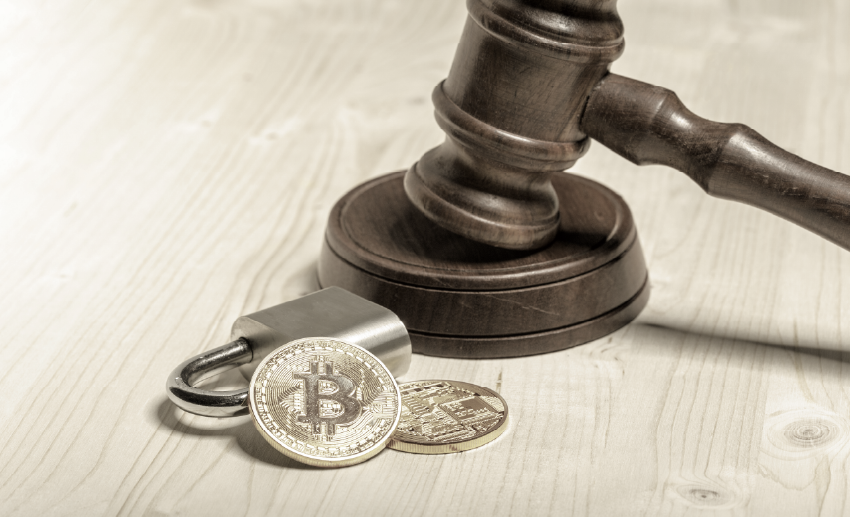 Um martelo de juiz em cima de uma mesa de madeira clara com um cadeado e uma moeda de bitcoin ao lado.