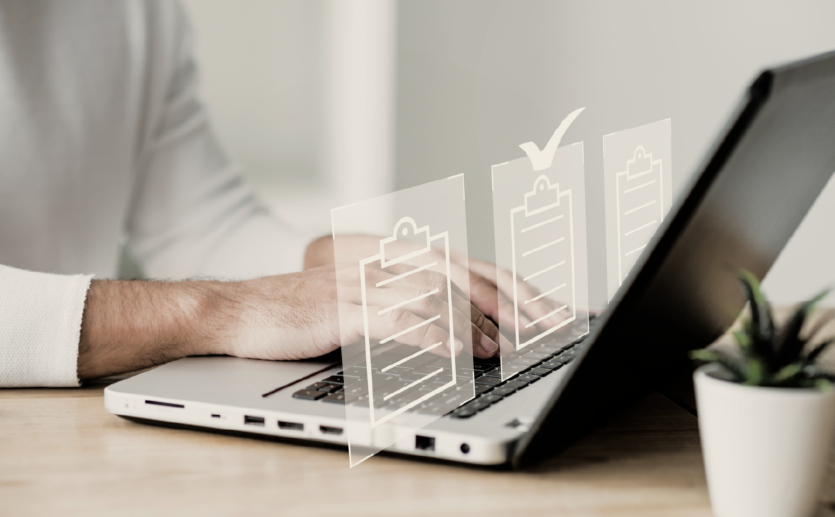 Close num laptop com uma mão masculina realizando cadastros representados com pastas virtuais com sinal de check
